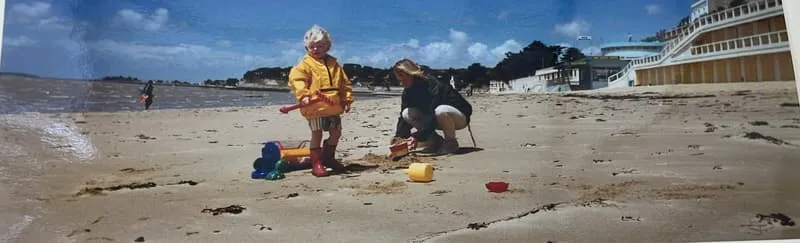 A small child with buckets and spades on the wide beach