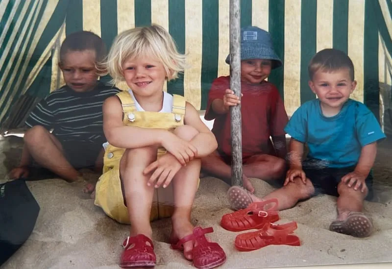 Four children sitting in the sand under a striped windbreak