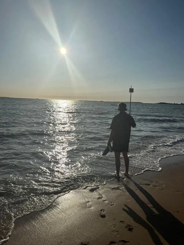Tess sitting on the sand, sun breaking through cloud