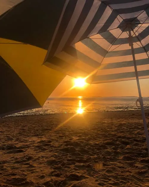 The sun setting over the water, seen from under a striped parasol